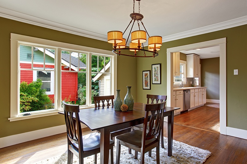 Dining room with wooden table set and rug on the hardwood floor. Room with green walls and white trim